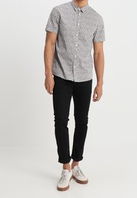 Camicia a maniche corte con bottoni, con motivo astratto in bianco e nero, abbinata a jeans neri slim e scarpe casual bianche.