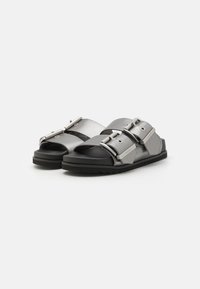 Sorte slidesandaler i sort med metalliske sølvstropper, med store justerbare spenner og strukturert fotseng for komfort. Gummisåle med mønster.