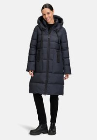 Giubbotto imbottito nero con cappuccio, trapuntatura verticale, zip frontale, tasche laterali e cordini regolabili sul cappuccio.