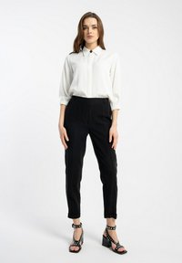 Biała bluzka z kołnierzykiem, czarne spodnie z wysokim stanem oraz czarne sandały na obcasie z akcentami w kropki. Gładki materiał, dopasowany krój.