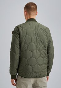 Giacca bomber trapuntata verde oliva con motivo esagonale, colletto e polsini a coste, e un dettaglio con applicazione sulla spalla sinistra.