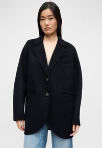 Mustast villast bleiser sisselõikega kraega, kahe eesmise tasku ja kaarekujuline äärega. Omadused: kaks nööpi ja lõdvestunud lõige.