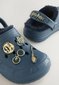 Blauwe klompen met een fuzzy voering, versierd met Harry Potter charme’s zoals een bril, bezemsteel, platform 9¾ en logo op de bandjes en de bovenkant van de schoenen.