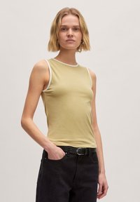 Licht olijfgroene mouwloze top met witte bies, gemaakt van zachte stof. Fitted ontwerp, gecombineerd met hoge zwarte jeans en een riem.