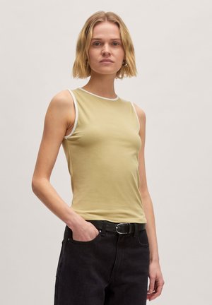 Licht olijfgroene mouwloze top met witte bies, gemaakt van zachte stof. Fitted ontwerp, gecombineerd met hoge zwarte jeans en een riem.