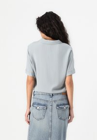 Light gray short-sleeve blouse with a folded collar, paired with a high-waisted denim skirt featuring back pockets and faded wash details.