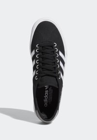 Musta kangaslenkkari valkoisilla raidoilla, pyöreällä varvastyynyllä ja metallisilla silmukoilla. Sisältää logon kummassakin kielessä ja harmaan yksityiskohdan kantapässä.