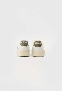 White sneakers with green accents and a beige sole. Features a textured fabric upper, padded heel, and embossed logo on the back.