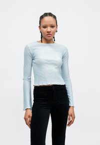 Top azul-claro de manga comprida canelado com bainha ondulada, combinado com calças pretas de cintura alta com bolsos. Design simples e ajustado.