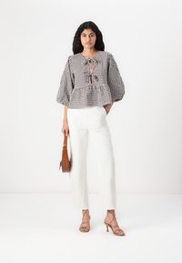 Top peplum a scacchi marrone e bianco, con dettaglio a chiave e maniche a sbuffo, abbinato a pantaloni bianchi a gamba larga e sandali beige con fasce.