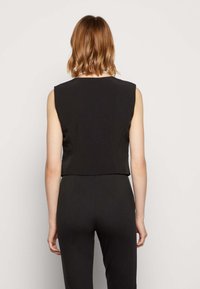 Haut noir sans manches au design court, présentant un tissu lisse et une silhouette épurée, offrant un look minimaliste.