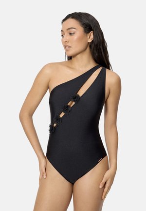 Mujer con un traje de baño negro de un solo hombro, con recortes diagonales y aplicaciones florales en la parte frontal.