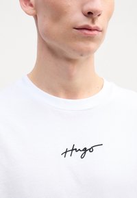 Hvid bomulds T-shirt med et sort broderet "Hugo" logo på brystet. T-shirten har en klassisk rund hals og korte ærmer.