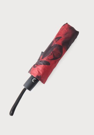 Parapluie compact plié avec un motif abstrait rouge et noir et une poignée noire avec dragonne sur un fond clair.