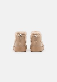 Tan ankle boots with faux fur lining, a rounded toe, and flat rubber sole. Features decorative silver hardware and pull tab at the heel.