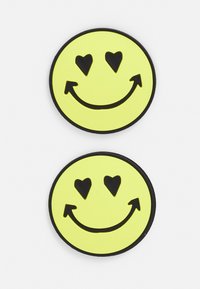Patches de rostos sorridentes amarelos apresentam contornos pretos, olhos em forma de coração e um sorriso curvado, feitos de um material macio e texturizado. Dois patches apresentados.