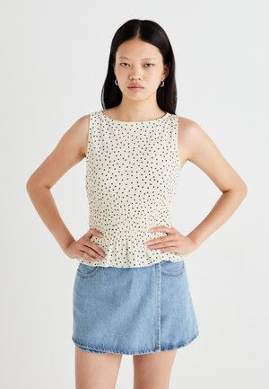 Mouwloze crèmekleurige top met zwarte stippen en een gegatherde taille, gecombineerd met een lichtblauwe denim minirok.