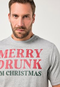 Grijze korte mouwen t-shirt met vetgedrukte rode en groene tekst die zegt "MERRY DRUNK I'M CHRISTMAS", met een relaxte pasvorm en ronde hals.