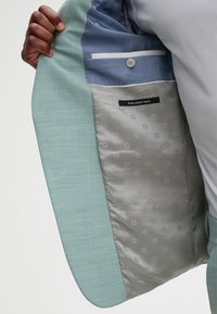 Light blue blazer with a smooth, slightly textured outer fabric. Interior features a patterned gray lining and blue accent material. Button detail visible.