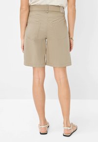 Shorts en coton beige avec une coupe décontractée, dotés d'un ourlet replié et de deux poches arrière. Présentés avec des sandales de couleur claire.
