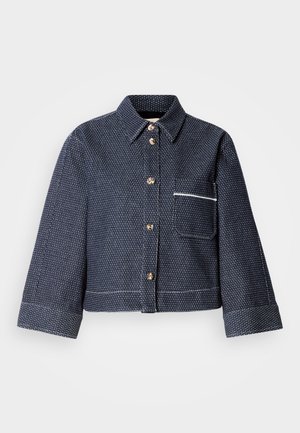 Tumesinise tekstuurse mustriga lühendatud pluus, kuldsete nööpide ja valge ääristusega rinnataskuga. Omaduseks on klassikaline krae ja üleskeeratud varrukad.