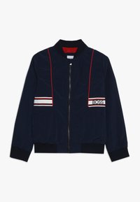 Chaqueta bomber navy con cremallera frontal, rayas verticales rojas, rayas horizontales blancas y rojas con el texto "BOSS" en el área del pecho.