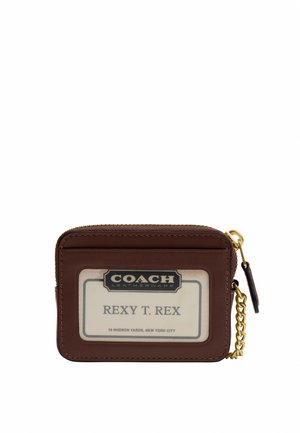 Porte-cartes Coach en cuir marron avec fenêtre d’identification transparente affichant "REXY T. REX" et détails de fermeture éclair et chaîne dorés sur fond blanc.