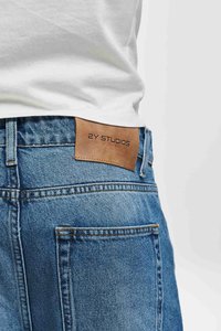 Lys blå denimjeans med et lærmerke bak på livet, med oransje søm og to baklommer. Klassisk avslappet passform.