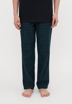 Pantalons de pyjama en flanelle verte à carreaux, fabriqués en tissu doux, avec des lignes verticales et horizontales en bleu foncé et violet, offrant une coupe décontractée.