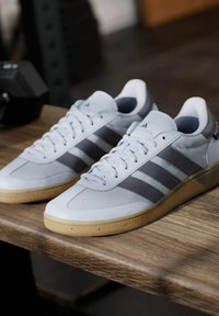 Lichtgrijze sportschoenen met donkergrijze strepen, rubberen gumzool, textuur bovenwerk en platte veters op een houten oppervlak.