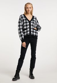 Cardigan în carouri alb-negru, cu decolteu în V, butoni frontali și buzunare. Purtați-l peste pantaloni negri și cizme negre cu șireturi.