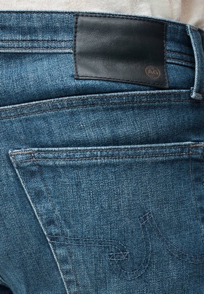 Μπλε τζιν παντελόνια με σκούρο δερμάτινο έμπλαστρο στη μέση. Διαθέτουν ορατές ραφές και πίσω τσέπη με καμπύλο σχέδιο.