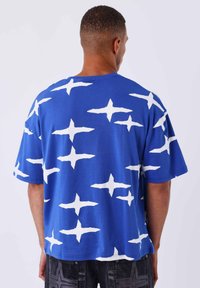 Camiseta azul de manga corta con un patrón abstracto de cruces blancas, confeccionada en tejido suave, con un corte relajado y escote redondeado.