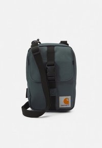 Bolsa tiracolo Carhartt em tecido verde-azulado com alça ajustável, aba frontal e patch com o logótipo. Apresenta uma forma rectangular e material durável.