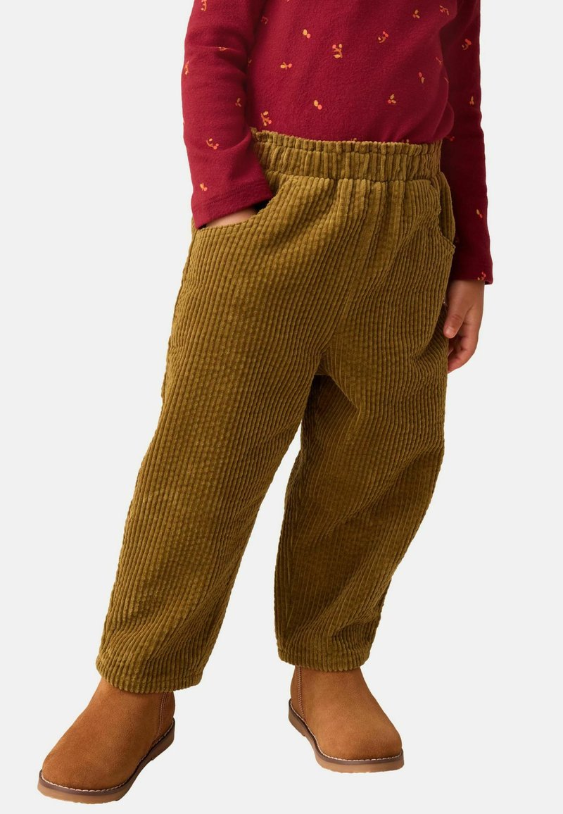 Pantalon en velours côtelé vert olive avec une texture striée, doté d'une taille élastique et de poches latérales, associé à des bottines brunes.