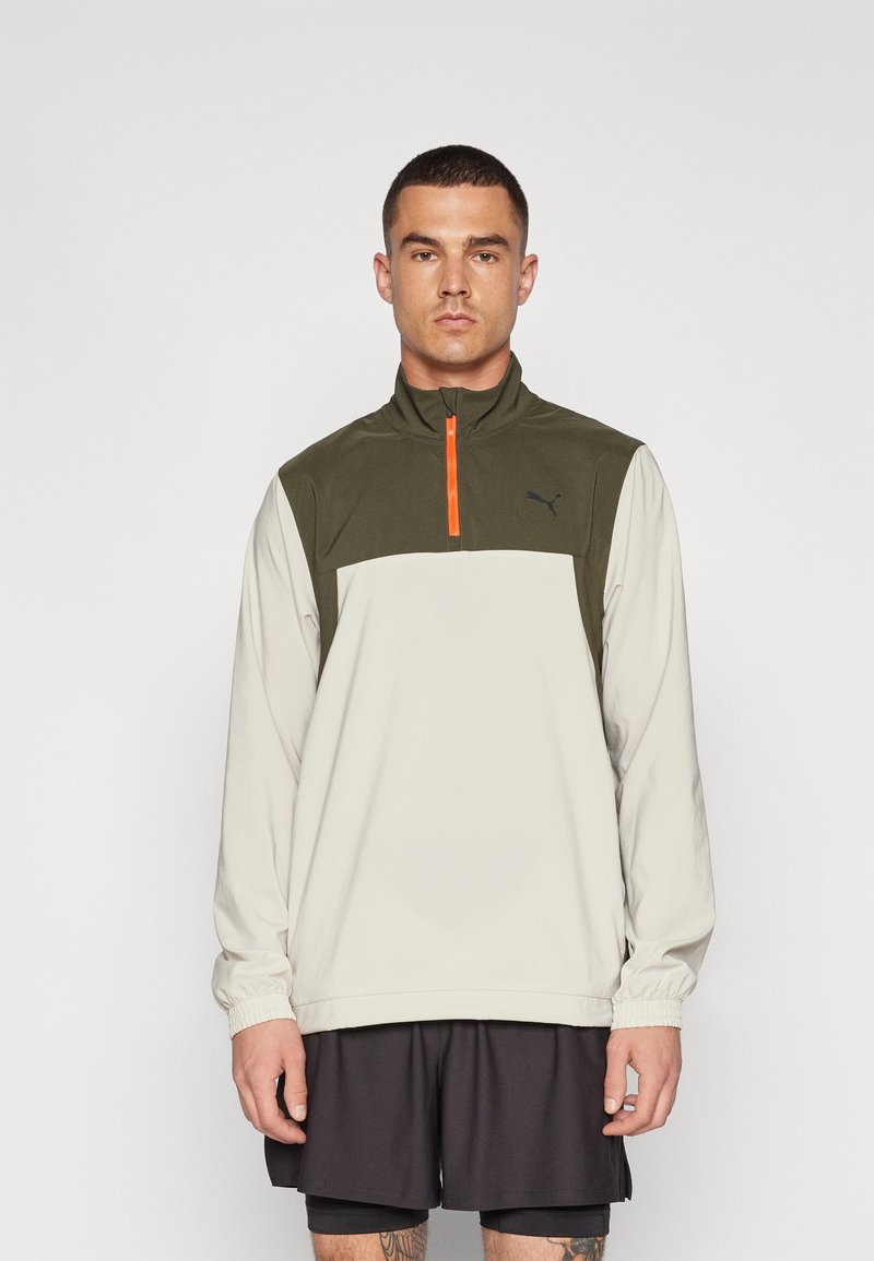 Kwart-rits pullover in olijfgroen en crème, met een oranje ritssluiting, elastische manchetten en een zwart logo op de borst. Lichtgewicht stof.