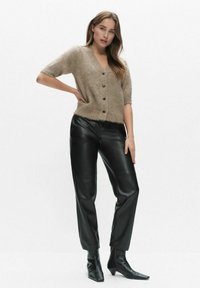 Ljusbrun, kortärmad cardigan med V-ringning och knappfront, kombinerad med svarta läderbyxor och spetsiga ankelboots.