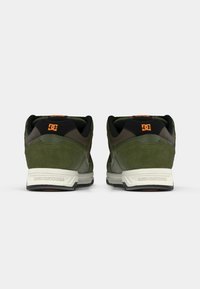 Green suede sneakers with black accents and orange logo. Features a padded collar, textured materials, and a white midsole with a black outsole.