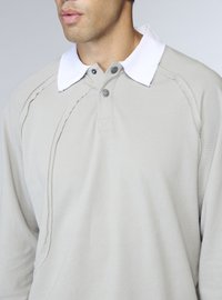 Polo a maniche lunghe in misto cotone beige chiaro, con colletto bianco, patta con bottoni e dettagli testurizzati sulle maniche.