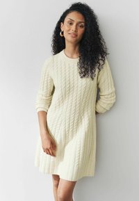 Robe en tricot jaune pâle, présentant un motif de cable texturé, un col rond et des manches longues. Tissu doux avec des détails côtelés.