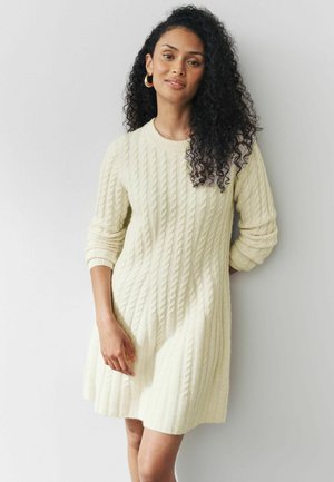 Strickkleid in sanftem Gelb mit strukturiertem Kabelmuster, Rundhalsausschnitt und langen Ärmeln. Weicher Stoff mit Rippendetails.