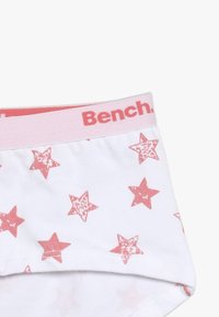 Shorts blancs avec un motif d'étoiles roses et une ceinture légère rose sur laquelle est inscrit "Bench." en rouge. Tissu doux.