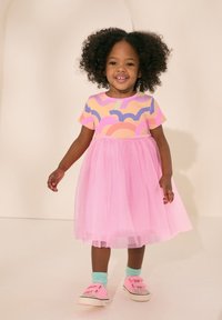 Kortärmad klänning med ett färgglatt mönstrat överstycke och en rosa tyllkjol, kombinerad med rosa sneakers och mintgröna strumpor.