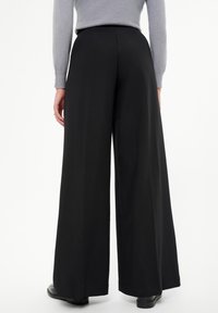 Pantalones negros de pierna ancha con una textura suave, con una cintura alta y una silueta fluida. Diseño simple y minimalista sin patrones visibles.