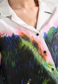 Knapp-up skjorta i lätt tyg med ett färgglatt, abstrakt mönster i gröna, blå och rosa nyanser; inkluderar svarta knappar och krage.