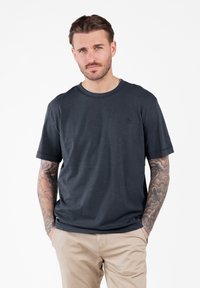 Camiseta gris oscuro hecha de tela suave, con cuello redondo, mangas cortas y un logo sutil en el área del pecho izquierdo.