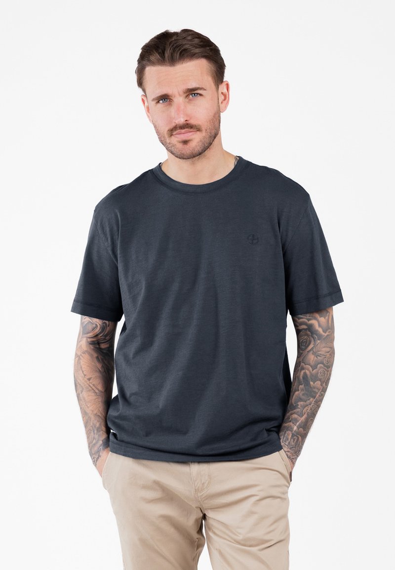 Camiseta gris oscuro hecha de tela suave, con cuello redondo, mangas cortas y un logo sutil en el área del pecho izquierdo.