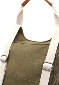 Plátěná taška olivově zelené barvy s krémovými popruhy, stříbrným kováním a kapsou na zip. Má zaoblený vršek a texturovaný povrch.