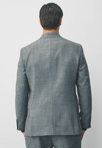 Grau wollener Blazer, strukturierter Stoff, klassischer Schnitt, abgestufte Revers, einfacher Schlitz, Knopfmitte mit drei Knöpfen, minimalistische Details. Ansicht von hinten.