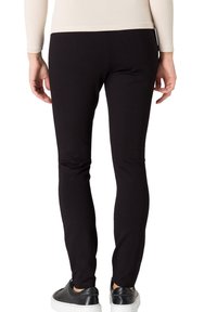 Leggings noirs en tissu extensible, avec une coupe slim et une texture lisse, accompagnés de baskets noires.